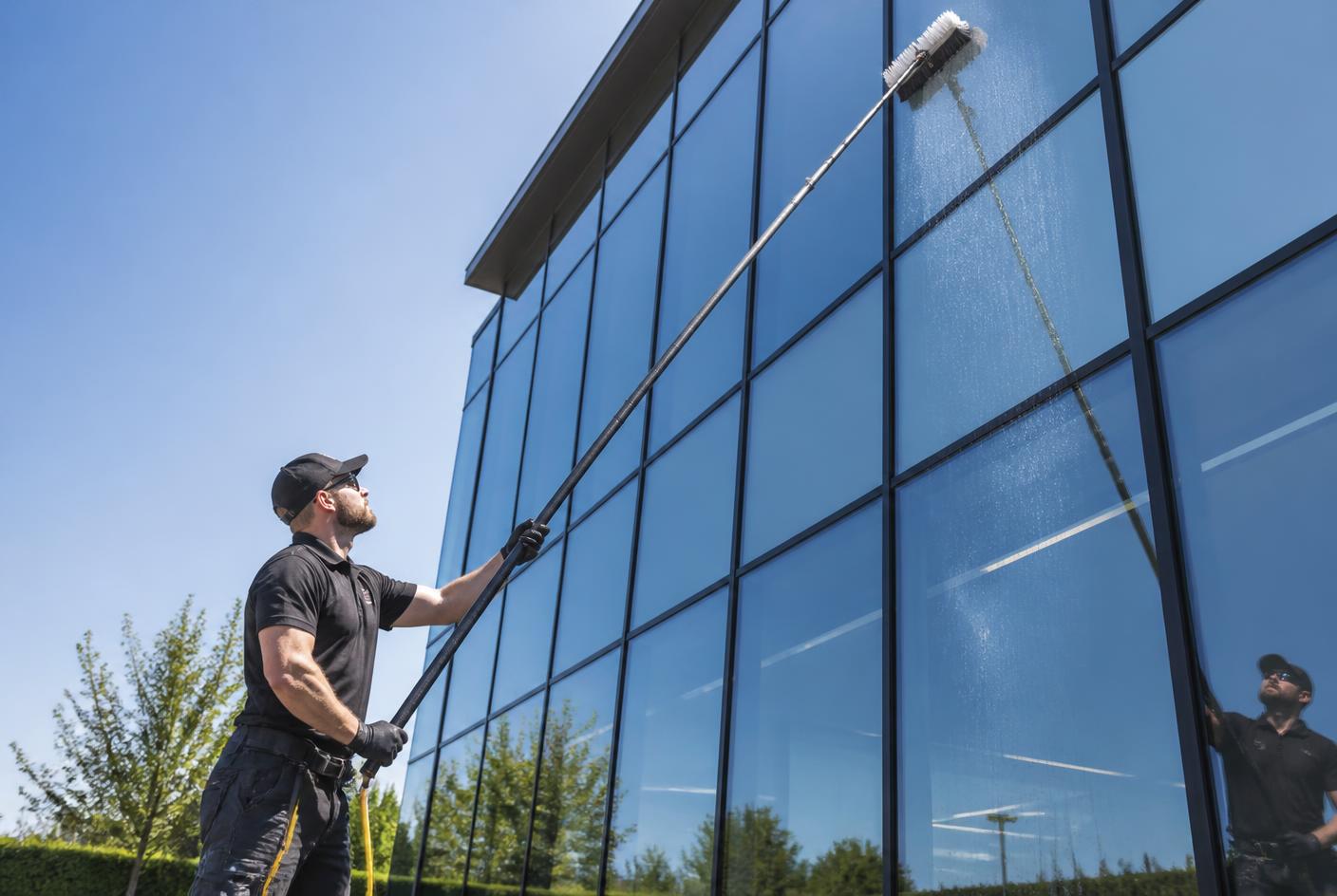 Glasreiniger reinigt eine Glasfassade eines Bürogebäudes mit einer Teleskopstange und Osmoseanlage