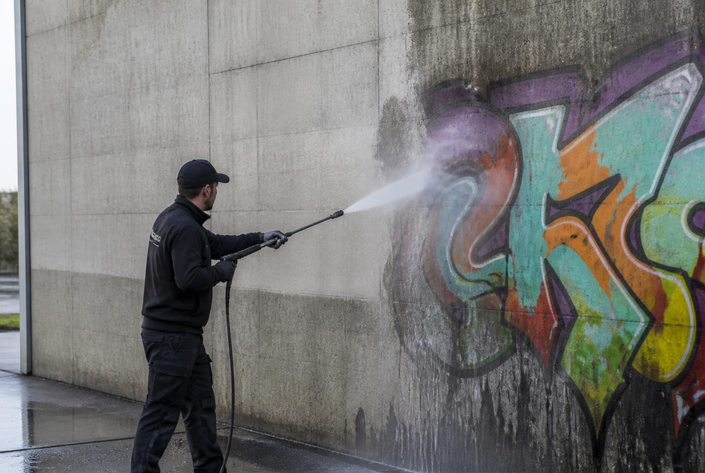 Mitarbeiter entfernt Graffiti mit Hochdruckreiniger von einer Betonwand
